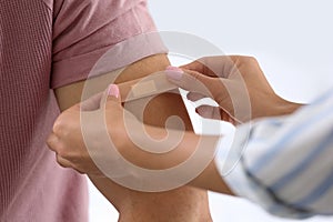 Woman applying adhesive  on man`s arm against light background, closeup