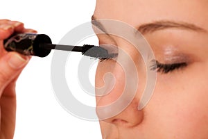 Woman applying black mascara on eyelashes.