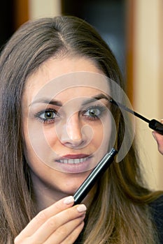 Woman applying black mascara on eyelashes with makeup brush. Make-up And Cosmetics Concept.