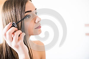 Woman applying black mascara on eyelashes with makeup brush. Young beautiful woman applying mascara makeup on eyes at bathroom.