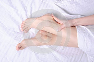 Woman applying body cream on her leg in bedroom massage closeup