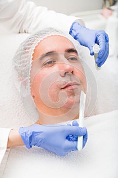 Woman applying with brush mask on man in spa salon