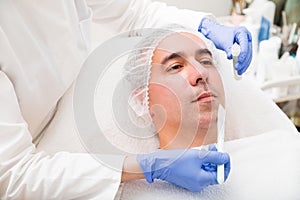 Woman applying with brush mask on man in spa salon