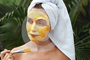 Woman Applying Clay Mask With Brush. Model In Bath Towel Using Skin Care Product For Oil Derma. photo