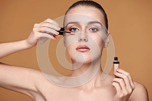 woman applying concealer under her eyes on beige background