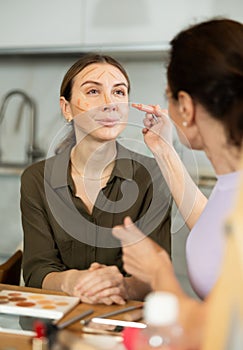 Woman applying contour makeup to female friend at home