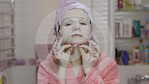 Woman applying cosmetic face mask in bathroom. Skincare spa. Facial mask