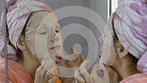 Woman applying cosmetic face mask in bathroom. Skincare spa. Facial mask