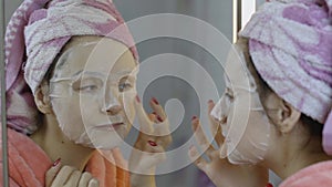 Woman applying cosmetic face mask in bathroom. Skincare spa. Facial mask