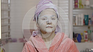 Woman applying cosmetic face mask in bathroom. Skincare spa. Facial mask