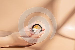 Woman applying cream on her hand on beige background with cosmetic products and hard shadows. Skin care treatment