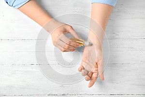 Woman applying essential oil on her wrist against white wooden background, top view