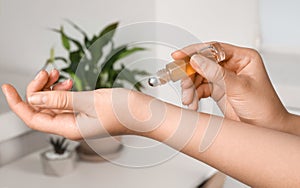Woman applying essential oil on wrist indoors
