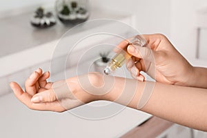 Woman applying essential oil on wrist indoors