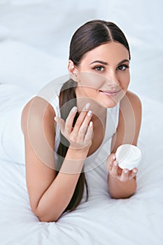 Woman Applying Facial Cream On Face Skin In White Interior