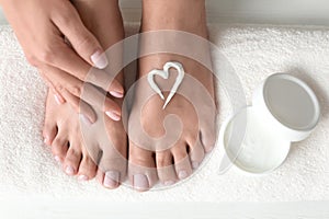 Woman applying foot cream on white towel, top view.