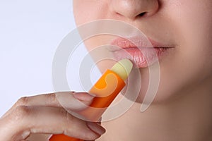 Woman applying hygienic lipstick on lips against white background, closeup