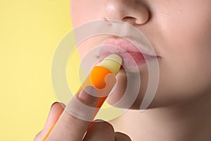 Woman applying hygienic lipstick on lips against yellow background