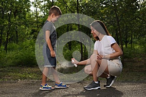 Woman applying insect repellent on her son`s leg in park. Tick bites prevention