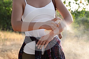 Woman applying insect repellent onto arm in park, closeup