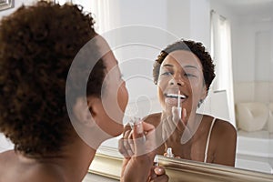 Woman Applying Lip Gloss In Mirror At Home