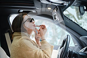 Woman applying lipstick wearing face mask while driving a car