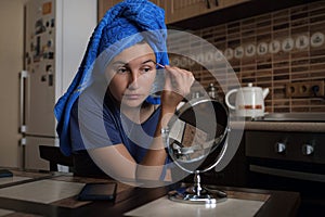 Woman applying make up beauty product with round makeup mirror at home kitchen