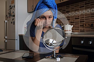 Woman applying make up beauty product with round makeup mirror at home kitchen