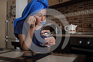 Woman applying make up beauty product with round makeup mirror at home kitchen