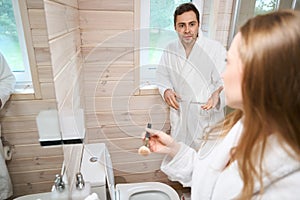 Woman applying makeup in the bathroom man looking at woman