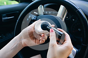 Woman is applying makeup in the car. Girl with face powder behind the wheel. Dangerous situation on the road. Possibility of