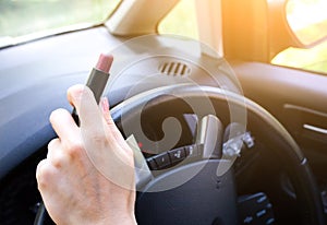 Woman is applying makeup in the car. Girl with lipstick behind the wheel. Dangerous situation on the road. Possibility of accident