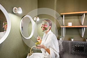 Woman applying mask on her face in the bathroom