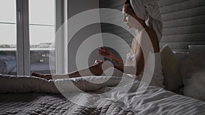 Woman applying moisturiser cream in bedroom