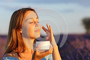 Woman applying moisturizer cream on cheek in lavender field