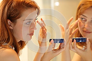 Woman applying moisturizer cream in eye bags at home