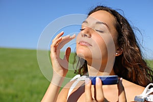Woman applying moisturizer cream in face in a field