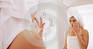 Woman applying moisturizer cream on her face in bathroom