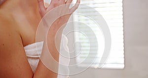 Woman applying moisturizer cream on her face in bathroom