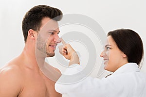 Woman applying moisturizer on man's nose