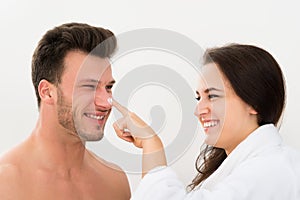 Woman applying moisturizer on man's nose