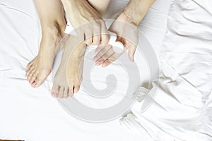 Woman applying moisturizing cream on her legs and feet in bedroom - body care concept