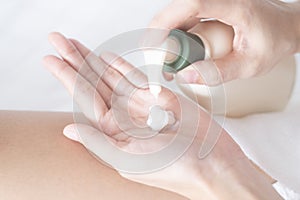 Woman applying moisturizing cream/lotion on hands on white bed, beauty concept