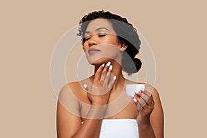 Woman Applying Moisturizing Cream to Her Neck Against Neutral Background