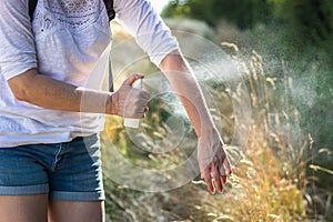 Woman applying mosquito repellent on hand in nature.