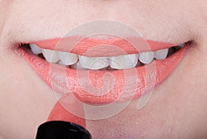 Woman applying orange lipstick on her lips
