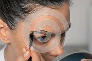 Woman applying paint on eyebrows making beauty procedure at home, closeup view.