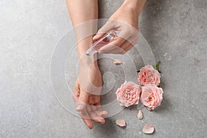 Woman applying rose essential oil on wrist and flowers at grey table