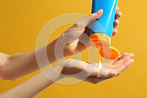 Woman applying sun protection cream on hand against background, closeup