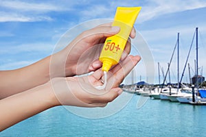 Woman applying sunscreen on her hand with blur boats docked